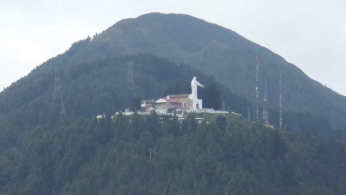 Fotografía del cerro de Guadalupe. Muestra un edificio blanco en la cima de una montaña con una estatua de la virgen, rodeado de un paisaje natural impresionante y cielo despejado.