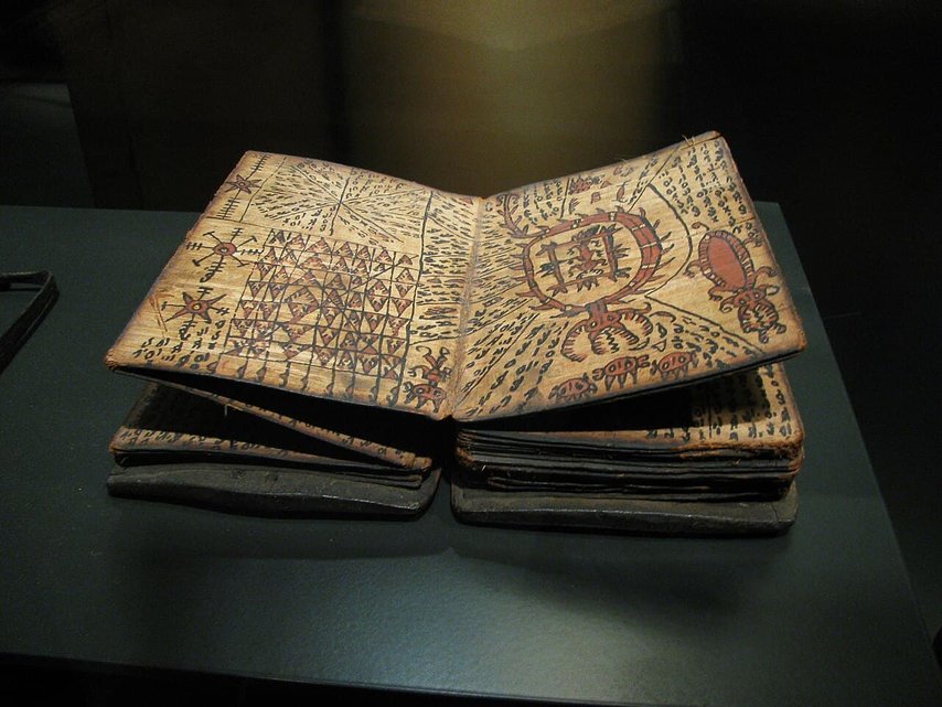 Manuscrito antiguo con símbolos y dibujos misteriosos. El libro abierto presenta páginas gruesas y manchadas, cubiertas de intrincados patrones, cuadrículas y glifos inusuales que parecen dibujados a mano. La página izquierda presenta formas geométricas y